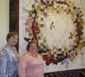 Ann Randolph (left) and Nancy Hiss stand in front of the group’s “Seasons of Pollination” quilt.