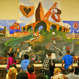 Students pull down the curtain to reveal their finished mural. The painting was designed and painted by Bridge Academy students with help from the Art Partners Studio.