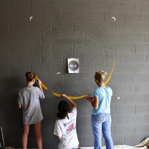 Emily Hadfield, Crystal Brau, and Lynné Filion begin work on the crest. They initially projected it onto the wall, tracing the lines.